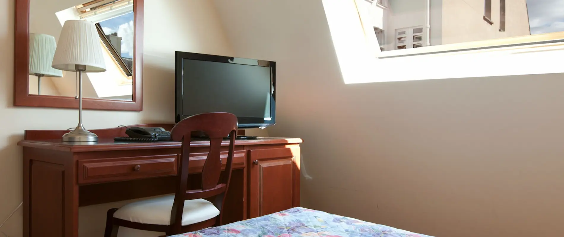 Bureau en bois avec miroir, lampe, télévision, situé près d'une fenêtre inclinée.