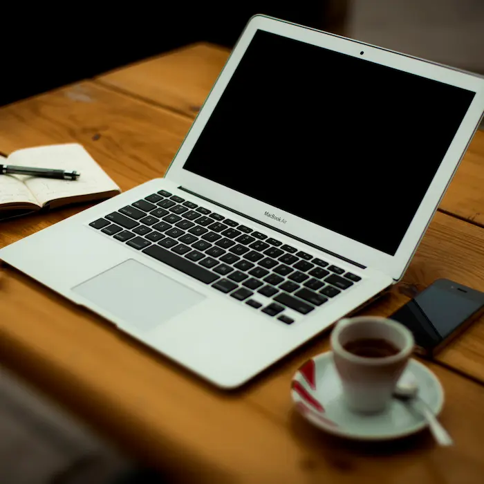 Ordinateur portable sur une table avec un carnet, un crayon et une tasse de café.