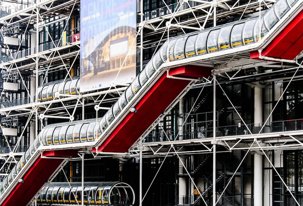 Structure moderne en métal et verre avec des escalators rouges et tuyaux extérieurs.