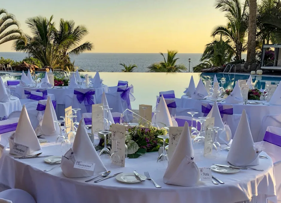 Mesas decoradas para un evento al aire libre con vista al mar al atardecer.