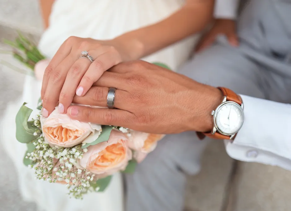Manos con anillos de boda sobre ramo de flores.