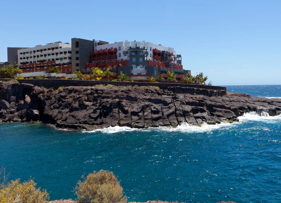 Edificio moderno en acantilado rocoso junto al mar azul, cielo despejado.