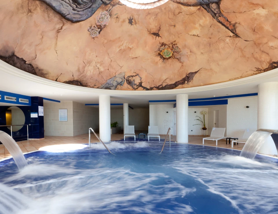 Piscina cubierta redonda con techo pintado y sillas blancas alrededor en un ambiente relajante.