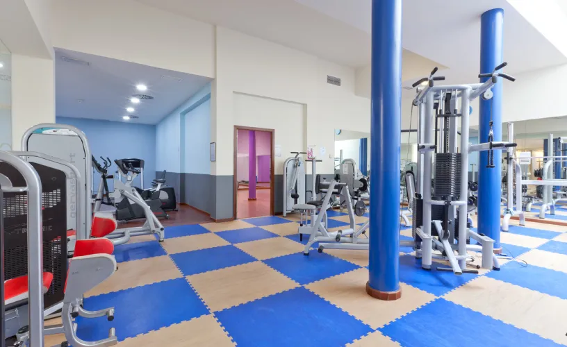 Gimnasio con máquinas de ejercicio sobre un suelo de baldosas azul y beige.