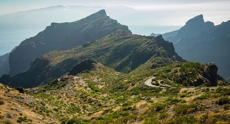 Montañas verdes con carretera serpenteante bajo cielo despejado.