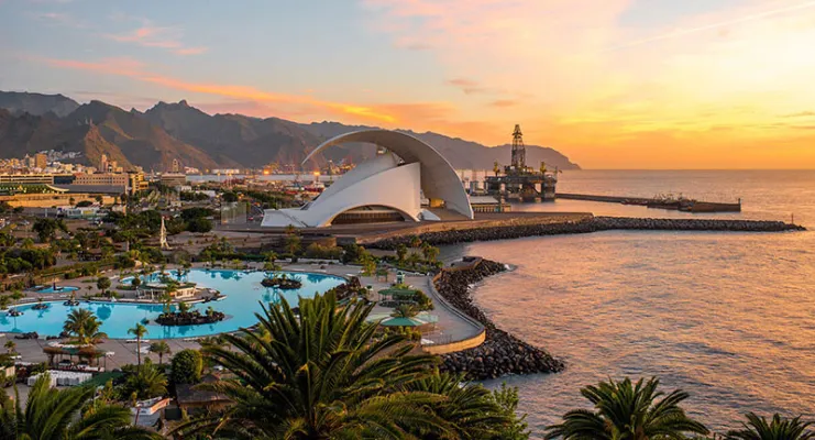 Auditorio futurista junto al mar al atardecer con montañas al fondo.