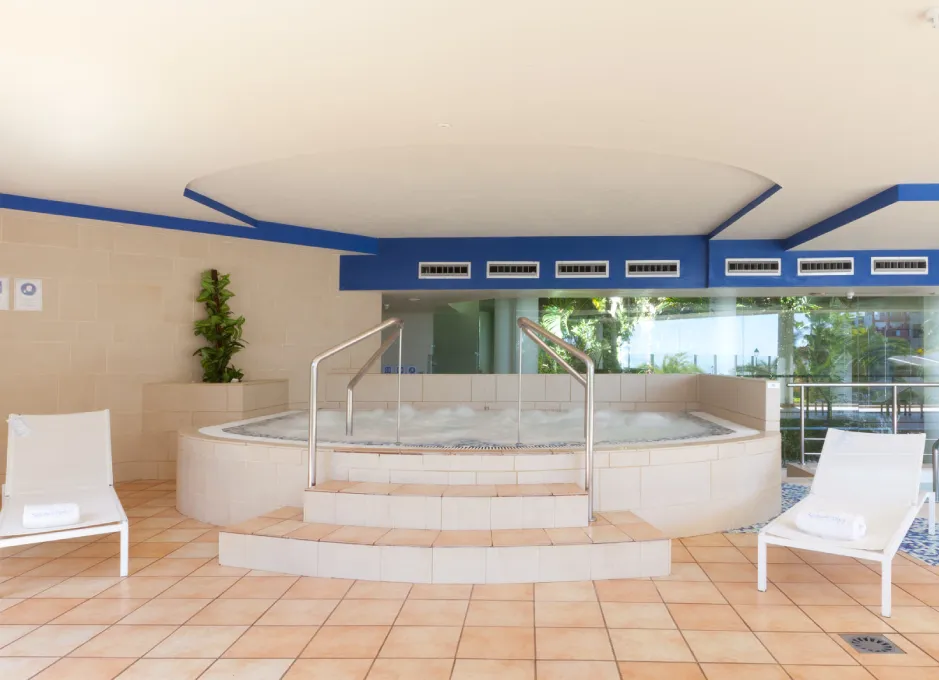 Jacuzzi interior con escaleras y dos sillas reclinables blancas en un espacio moderno y luminoso.