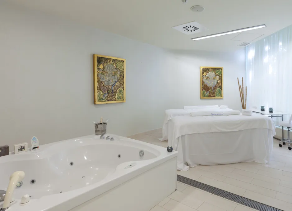 Sala de spa con jacuzzi, camilla de masaje y dos cuadros en la pared.