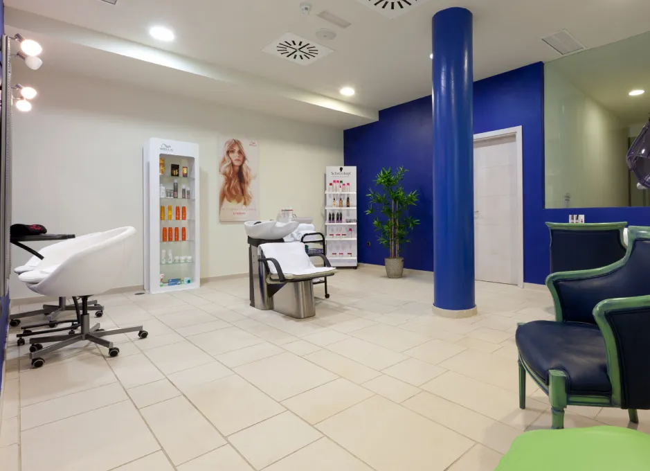 Salón de belleza moderno con sillas blancas y productos para el cabello exhibidos en estantes.