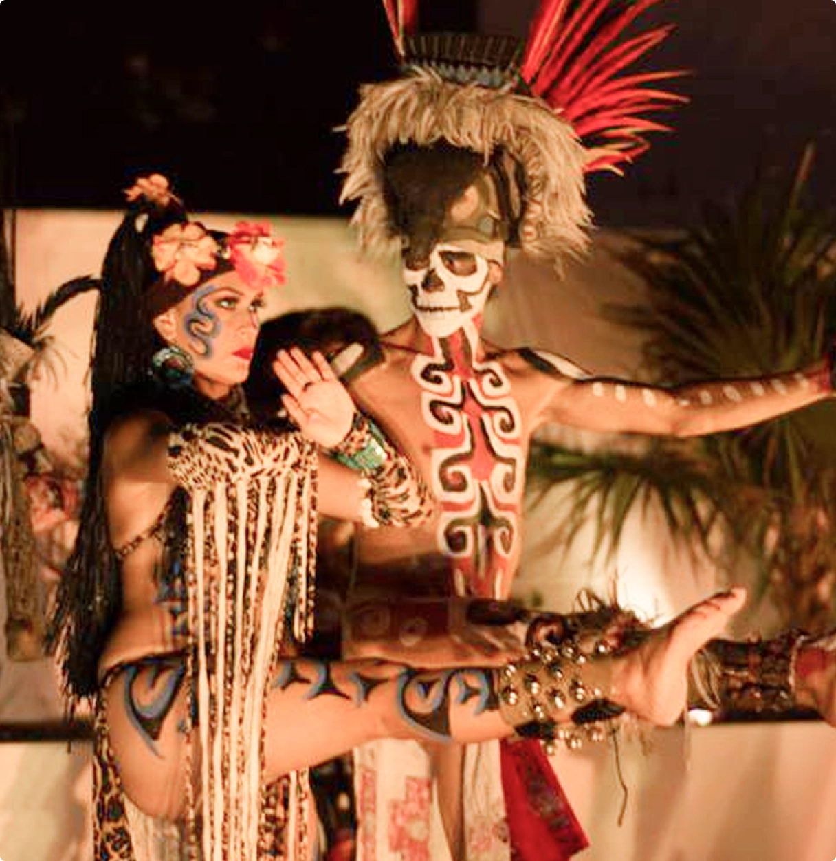 Pareja en traje de danza tradicional, con pintorescos atuendos y pintura corporal. Fondo de plantas.