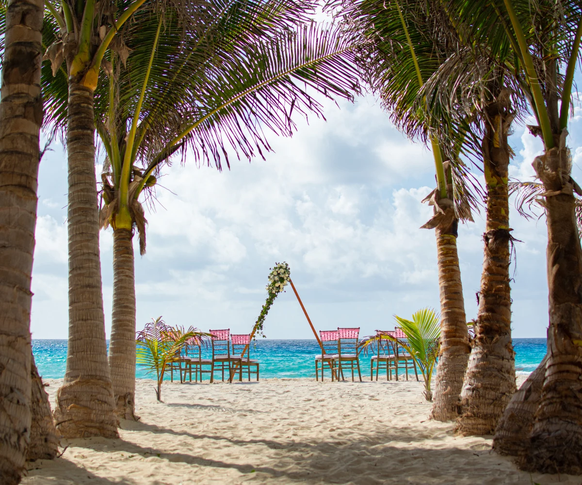 Boda en la playa con arco floral y sillas frente al mar azul turquesa.