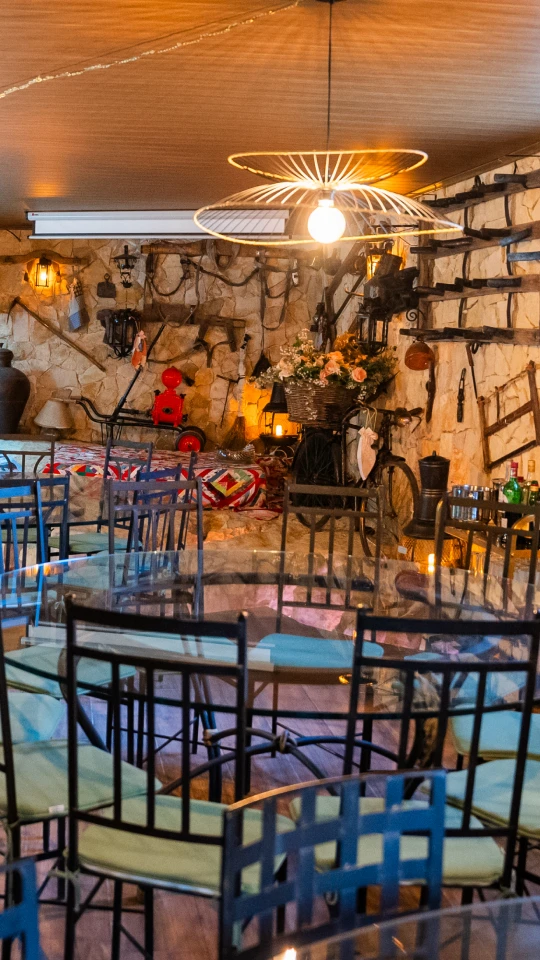 Sala decorada com tema rústico, mesas de vidro, cadeiras pretas e luz suave.