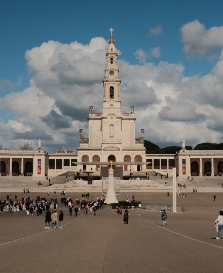 Pessoas em frente a uma grande basílica sob um céu azul com nuvens.