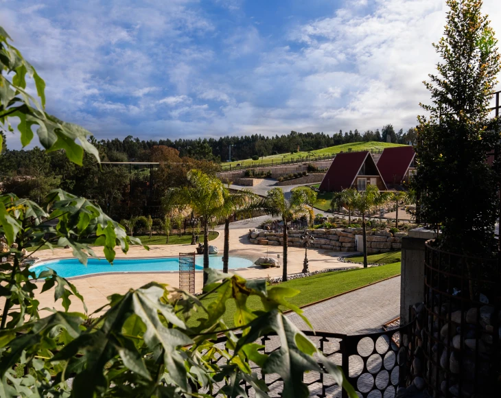 Vista de um resort com piscina, chalés e natureza ao redor, sob um céu parcialmente nublado.