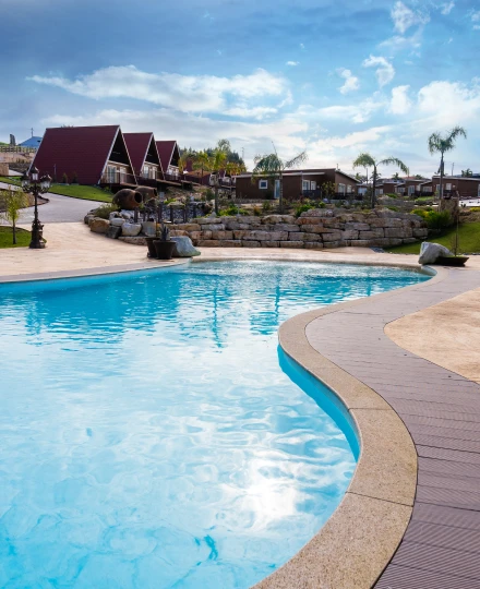 Piscina clara com chalés ao fundo e céu parcialmente nublado.