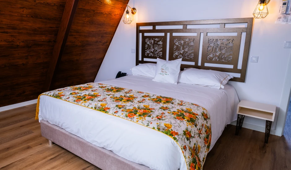 Quarto aconchegante com cama de casal decorada com colcha floral e luminárias de parede.