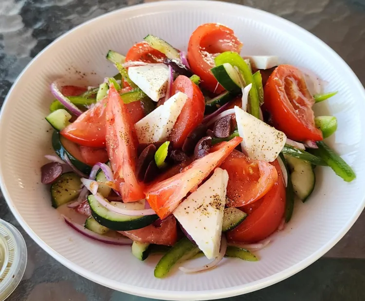 Ensalada griega con tomate, queso, pepino, cebolla morada, pimientos y aceitunas en un tazón blanco.