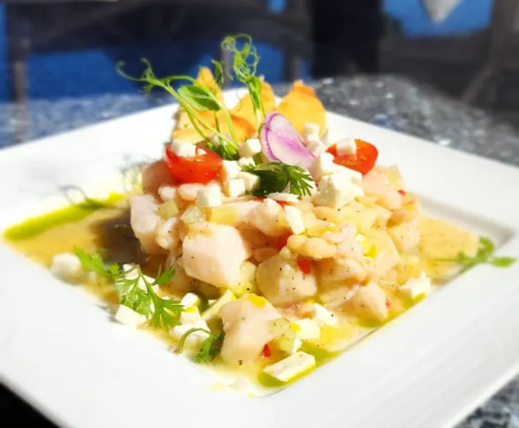 Plato de ceviche con queso, tomate cherry y cebolla morada decorado con hierbas frescas.