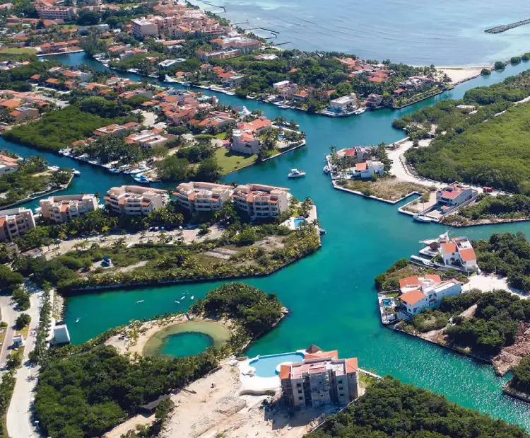 Vista aérea de una zona residencial junto a un canal de agua turquesa, rodeada de vegetación.