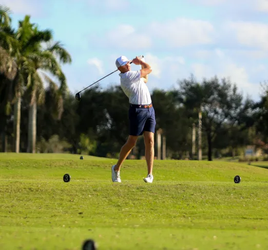 Persona jugando golf en un campo rodeado de árboles, vistiendo ropa deportiva.