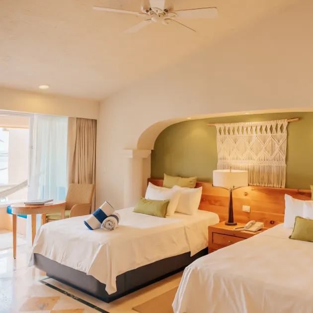 Habitación con dos camas, decoración acogedora, lámpara, y balcón con cortinas abiertas.