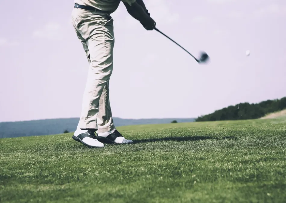 Persona jugando golf en un campo verde, capturada en medio del swing del palo.