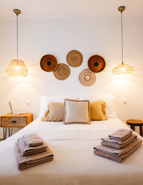 Quarto decorado com cama arrumada, luminárias de fibra e cestos na parede.