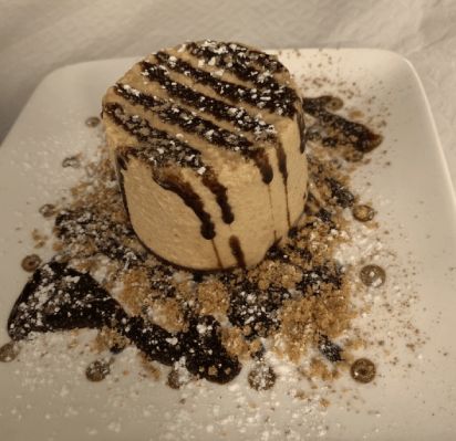 Sobremesa com calda de chocolate e açúcar de confeiteiro, servida em prato quadrado branco.