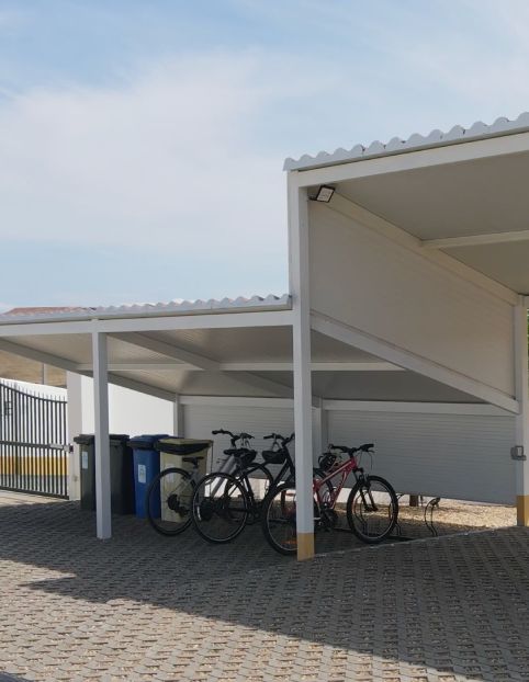 Estacionamento coberto com bicicletas e latas de lixo coloridas ao lado.