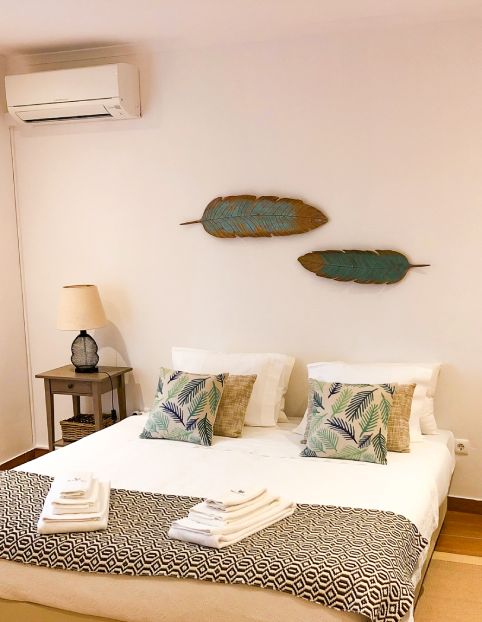 Quarto com cama de casal, decoração tropical e ar-condicionado na parede.