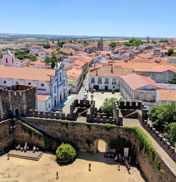Vista aérea de cidade com arquitetura histórica e muralhas de castelo em primeiro plano.