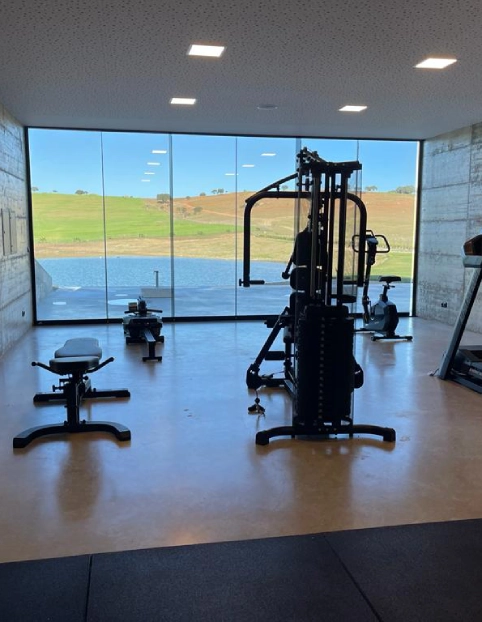 Sala de ginástica moderna com vista panorâmica para campos verdes através de grandes janelas.