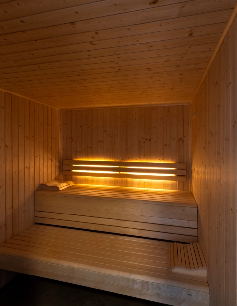 Sauna de madeira iluminada, com bancos em dois níveis e toalhas dobradas sobre eles.