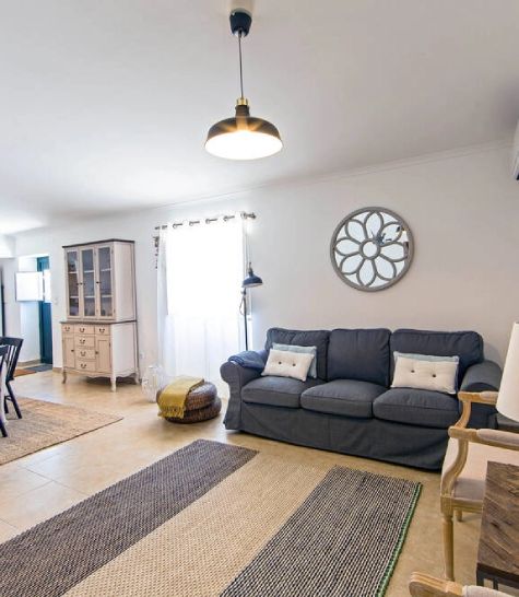 Sala de estar iluminada, com sofá cinza, tapetes e decoração minimalista em cores neutras.