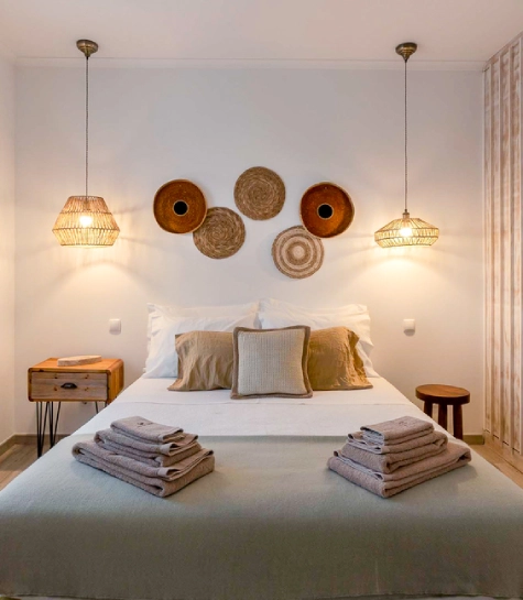 Quarto com cama arrumada, luminárias pendentes e decoração de cestos na parede.
