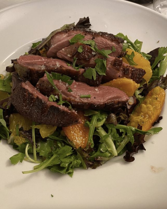 Salada com fatias de carne, folhas verdes e gomos de laranja em prato branco.