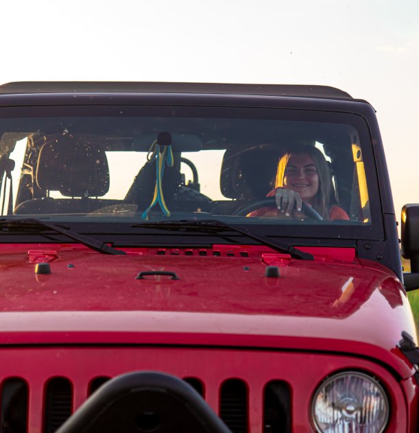 Pessoa sorrindo ao volante de um jipe vermelho sob luz do fim de tarde.