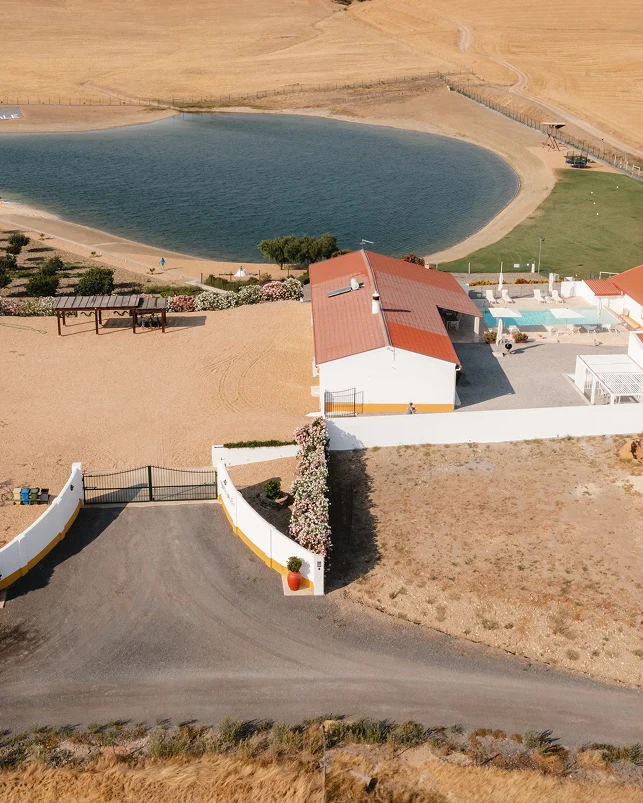 Vista aérea de uma propriedade rural com casa, lago e piscina, cercada por campos secos.