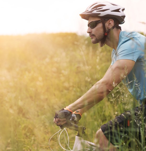 Ciclista de capacete e óculos em estrada rural com gramado ao sol.