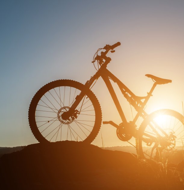 Sombra de bicicleta contra o pôr do sol, vista de lado em um terreno elevado.