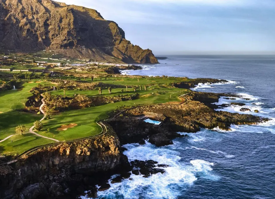 Vista aérea de campo de golf junto a un acantilado rocoso y el océano al fondo.