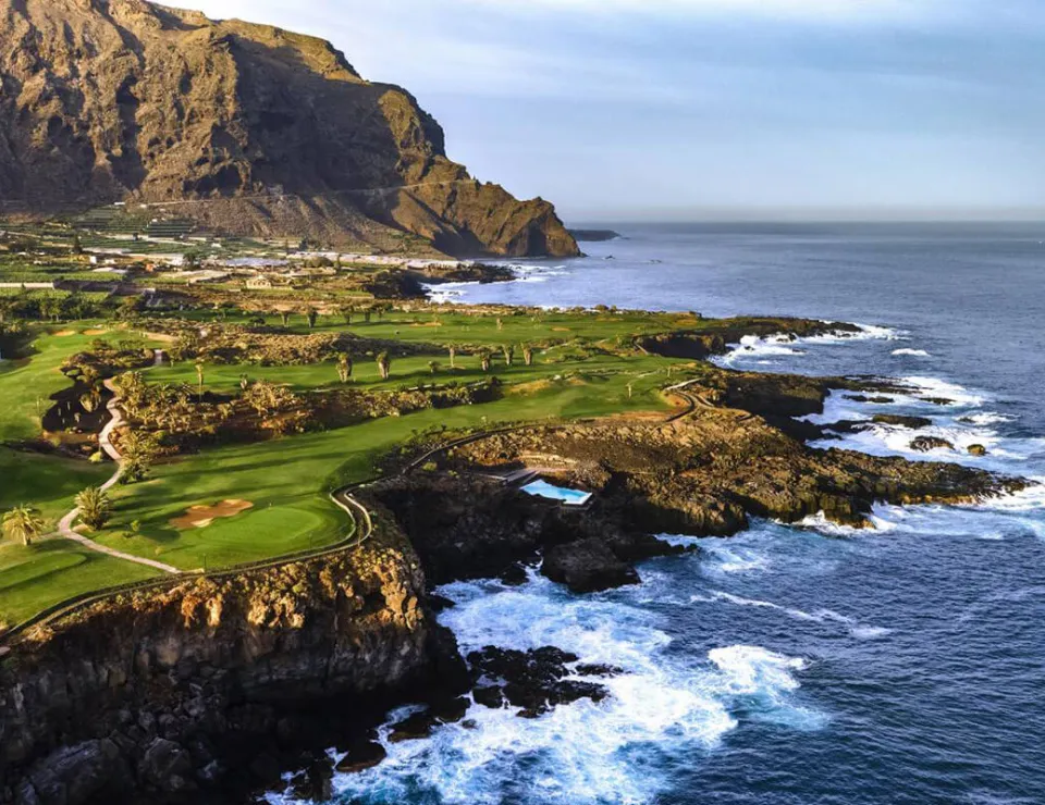 Costa rocosa y campo verde junto al mar bajo un acantilado imponente.