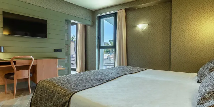 Habitación de hotel con cama, escritorio, televisión y ventana con cortinas.