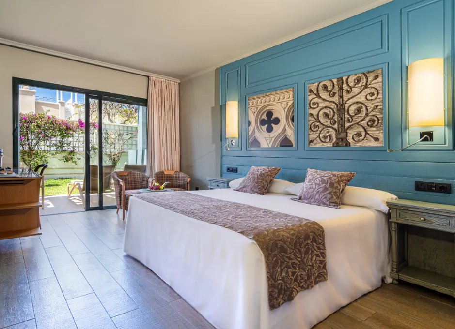 Habitación de hotel luminosa, cama doble, decoración azul y terraza con vista al jardín.