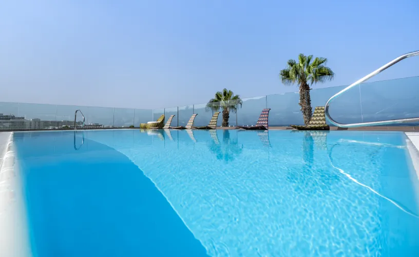 Piscina en la azotea con tumbonas y palmeras, cielo despejado.
