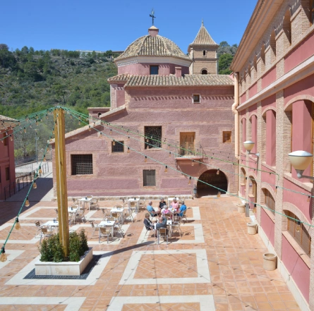 Patio al aire libre con mesas y sillas, rodeado de edificios de estilo clásico y luces colgantes.