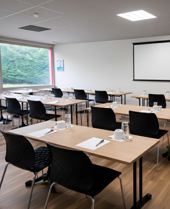 Aula vac&iacute;a con mesas dispuestas en filas, pizarra y ventana con vista a &aacute;rboles.
