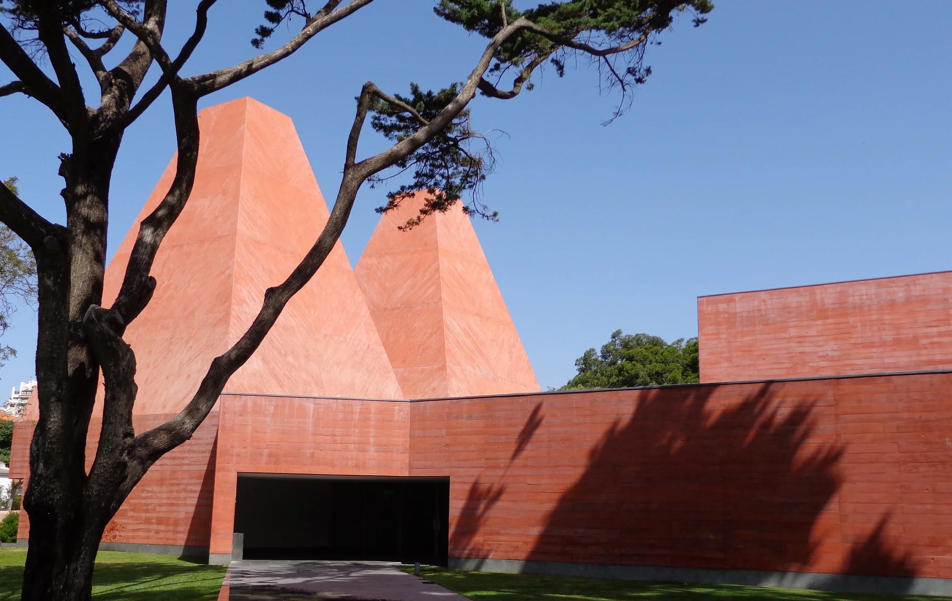 Modern red brick building with geometric shapes and trees on a clear day.