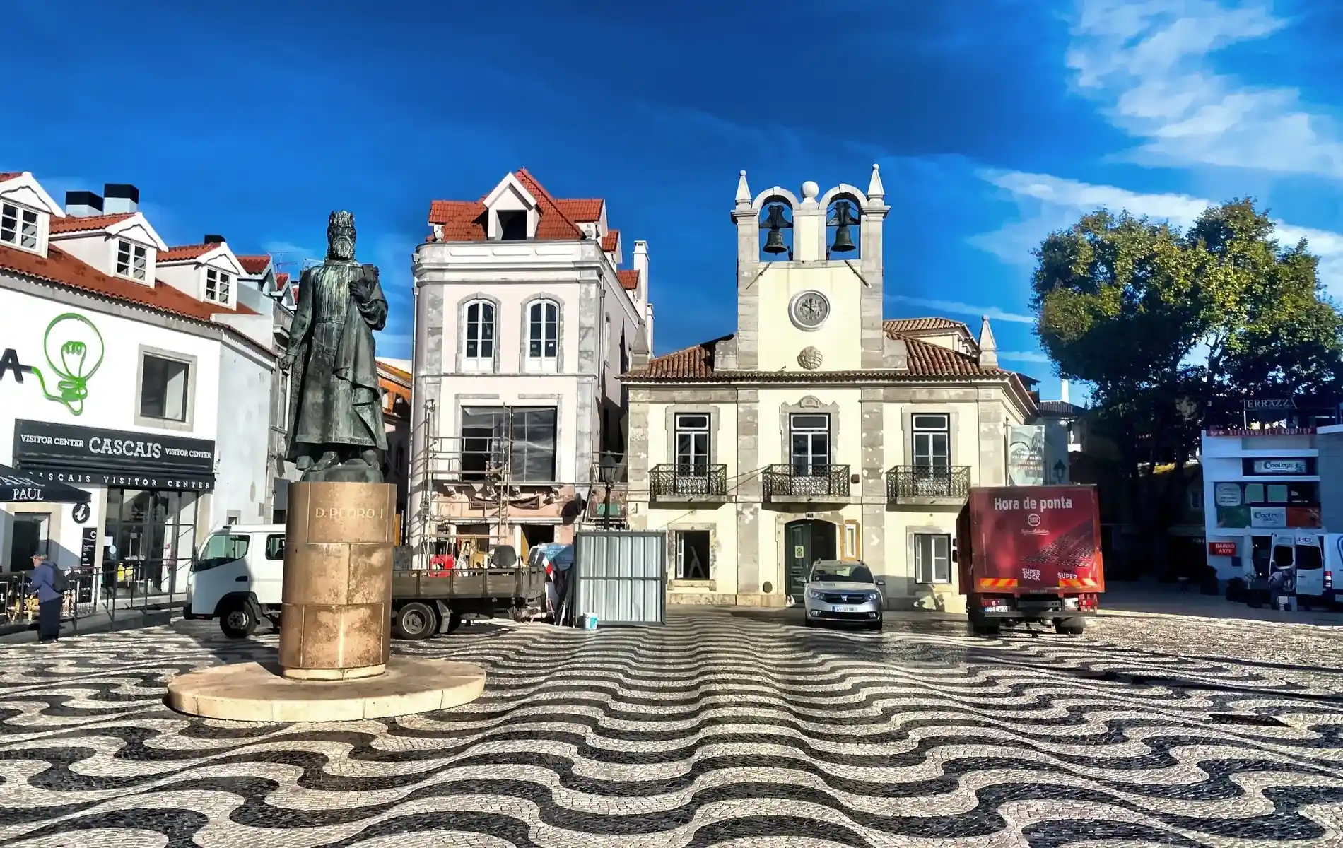 Statue and wavy patterned plaza in front of historic buildings under a clear blue sky.