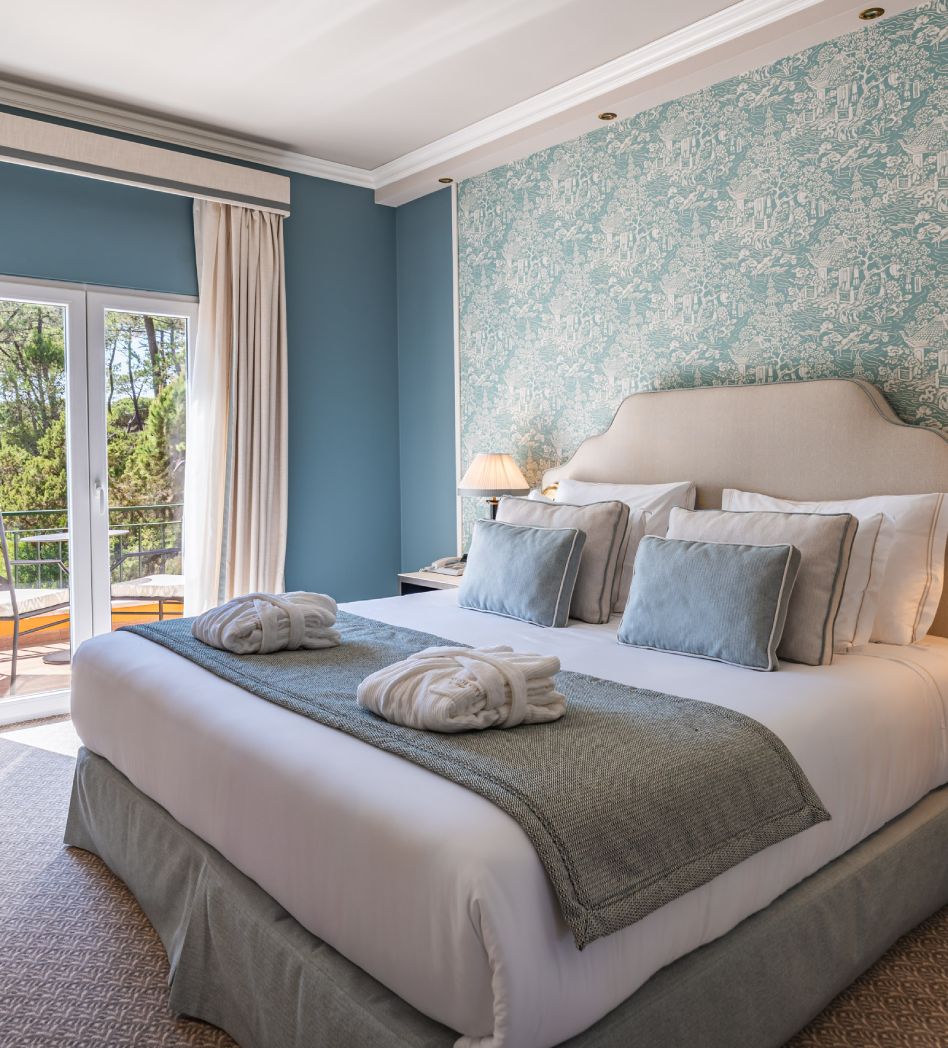 Cozy hotel room with a large bed, blue accents, and a view of trees from the balcony.